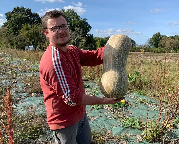 Agriculteur souriant tenant une courge allongée dans un champ ensoleillé à Villedieu-sur-Indre près de Châteauroux en Indre 36